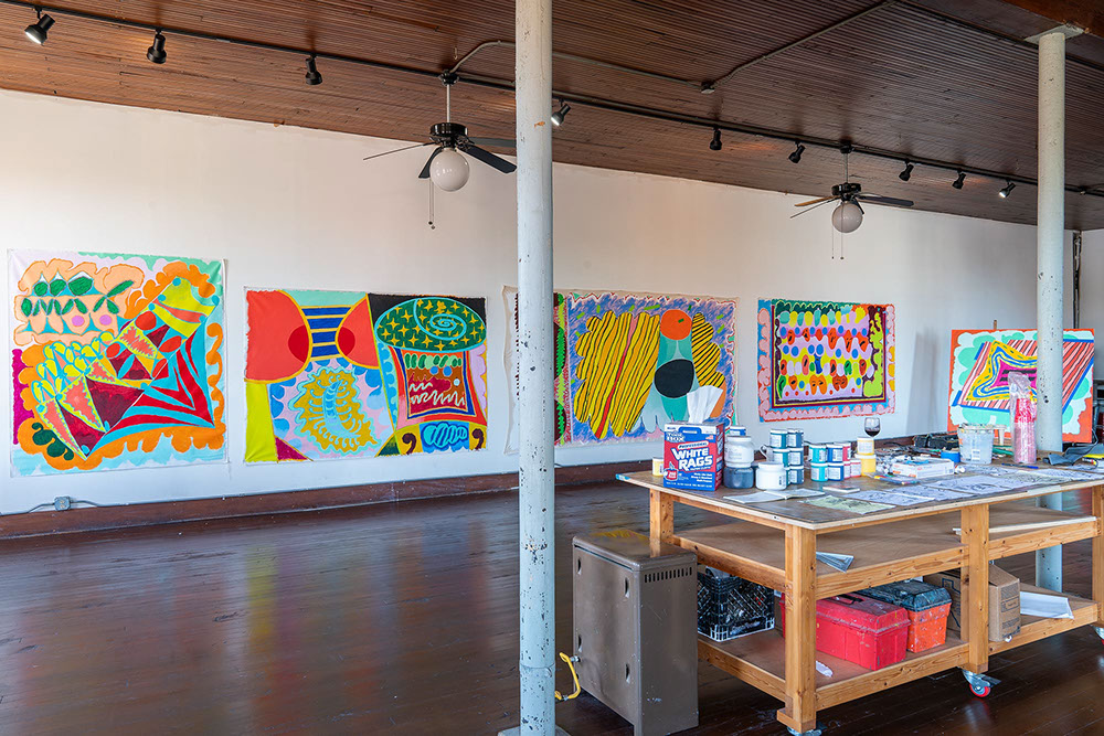 Second floor studio at one hundred west artist residency with worktable in foreground and paintings on the wall