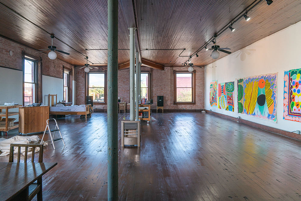 second floor studio at one hundred west corsicana artist residency with a bed on the left and large windows and a long wall on the right